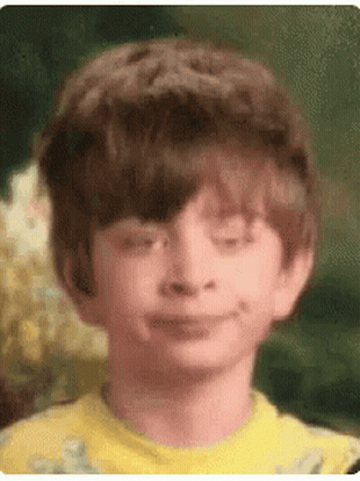 A Young Boy In A Yellow Shirt Is Smiling With His Eyes Closed . GIF