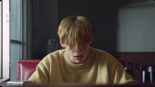 A Young Boy In A Yellow Sweater Sits At A Table GIF