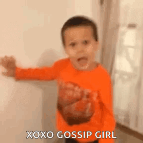 A Young Boy In An Orange Shirt Is Standing In Front Of A White Wall And Says `` Xoxo Gossip Girl '' . GIF