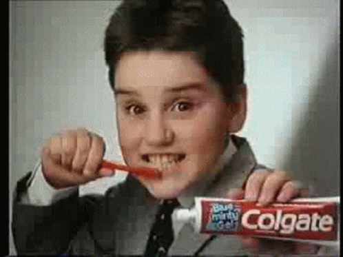 A Young Boy Is Brushing His Teeth With A Tube Of Colgate Toothpaste . GIF
