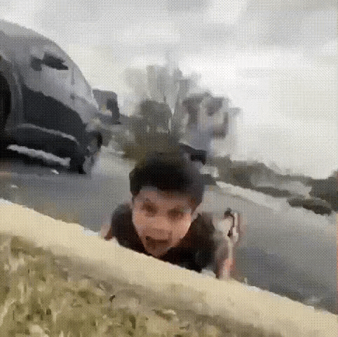 A Young Boy Is Crawling On The Side Of A Road In Front Of A Car . GIF