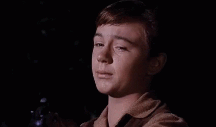A Young Boy Is Crying In A Dark Room While Holding A Bottle . GIF