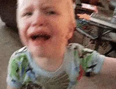 A Young Boy Is Crying On The Floor While Wearing A Dinosaur Shirt . GIF