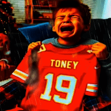 A Young Boy Is Crying While Holding Up A Toney 19 Jersey GIF
