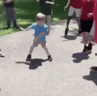 A Young Boy Is Dancing On A Sidewalk While A Group Of People Watch . GIF
