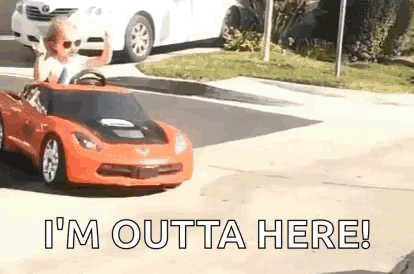 A Young Boy Is Driving A Toy Car Down A Street . GIF