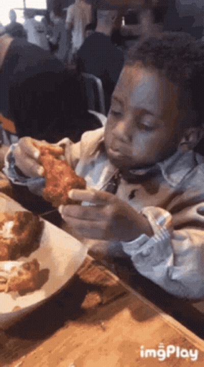 A Young Boy Is Eating A Chicken Wing At A Restaurant . GIF