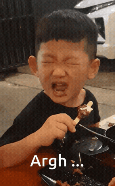 A Young Boy Is Eating A Skewer Of Food And The Word Argh Is On The Bottom GIF