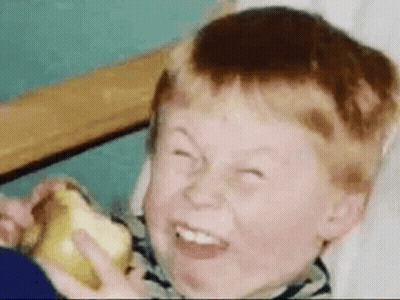 A Young Boy Is Eating An Apple And Making A Funny Face . GIF
