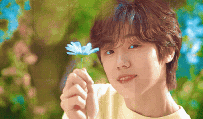 A Young Boy Is Holding A Blue Flower In His Hand And Smiling . GIF