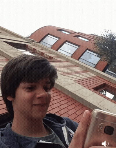 A Young Boy Is Holding A Cell Phone In Front Of A Building GIF
