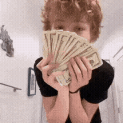 A Young Boy Is Holding A Fan Of Money In Front Of His Face . GIF