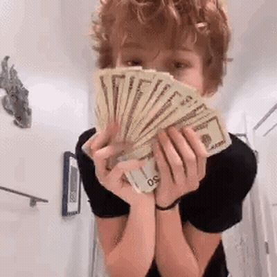 A Young Boy Is Holding A Fan Of Money In His Hands . GIF
