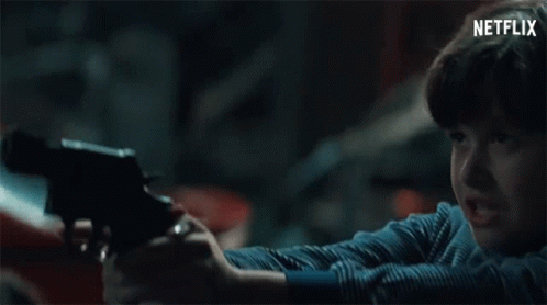A Young Boy Is Holding A Gun In A Dark Room With A Netflix Logo Behind Him . GIF