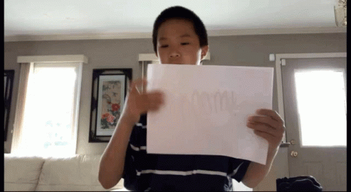 A Young Boy Is Holding A Piece Of Paper That Says " Mom " GIF