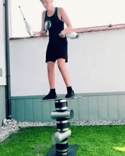 A Young Boy Is Juggling Balls While Standing On A Stack Of Cylinders . GIF