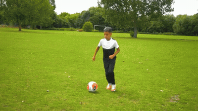 A Young Boy Is Kicking A Soccer Ball On A Field GIF