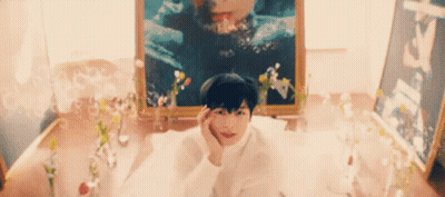 A Young Boy Is Laying In A Bathtub With Flowers And A Picture Of A Woman In The Background . GIF