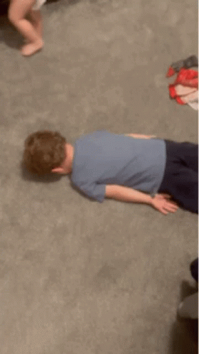 A Young Boy Is Laying On The Floor In A Room GIF