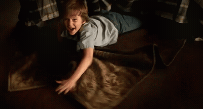 A Young Boy Is Laying On The Floor Playing With A Blanket And Smiling . GIF