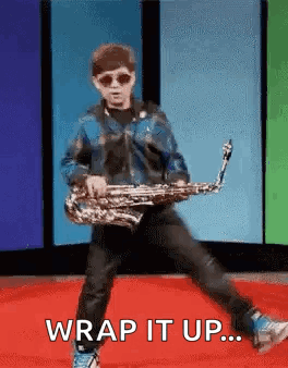 A Young Boy Is Playing A Saxophone On A Red Carpet While Wearing Sunglasses And A Blue Jacket . GIF