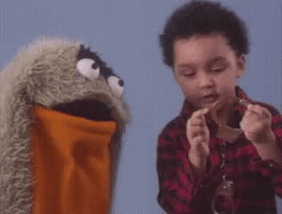 A Young Boy Is Playing With A Puppet While Holding A Piece Of Paper . GIF