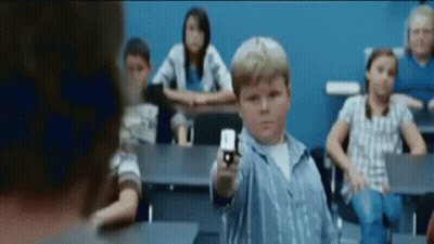 A Young Boy Is Pointing A Gun In A Classroom With Other Children GIF