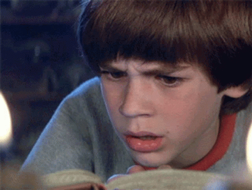A Young Boy Is Reading A Book And Making A Funny Face GIF