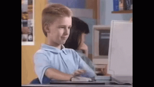 A Young Boy Is Sitting At A Desk Looking At A Computer Screen . GIF