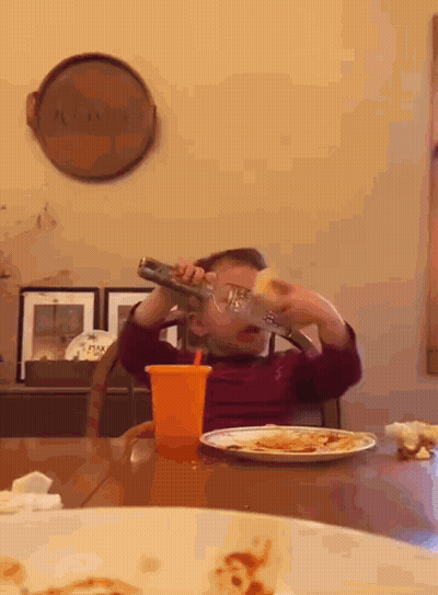 A Young Boy Is Sitting At A Table Drinking From A Bottle With A Straw GIF