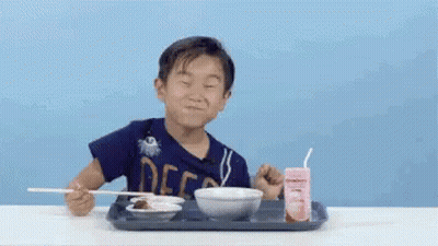 A Young Boy Is Sitting At A Table Eating Food With Chopsticks And A Strawberry Milk . GIF