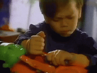 A Young Boy Is Sitting At A Table Playing With A Toy Dinosaur . GIF