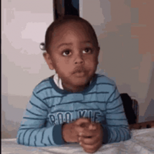 A Young Boy Is Sitting At A Table With His Hands Folded In Front Of Him . GIF