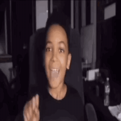 A Young Boy Is Sitting In A Chair And Making A Peace Sign With His Hand . GIF