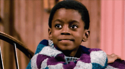 A Young Boy Is Sitting In A Chair Wearing A Purple And Blue Plaid Sweater GIF