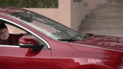 A Young Boy Is Sitting In A Red Car With A Citytv Sticker On The Side . GIF