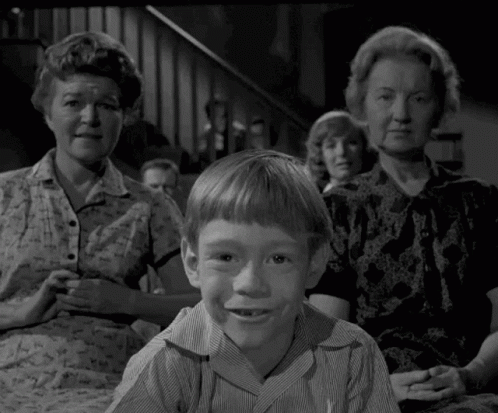 A Young Boy Is Sitting In Front Of A Group Of People . GIF