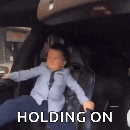 A Young Boy Is Sitting In The Back Seat Of A Car With The Words " Holding On " Above Him GIF