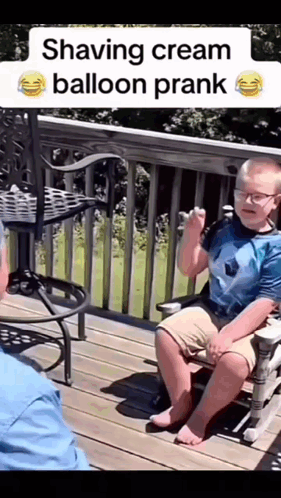 A Young Boy Is Sitting On A Deck Talking To An Older Man Who Is Shaving Cream Balloon Prank .. GIF