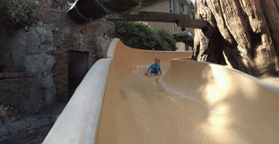 A Young Boy Is Sliding Down A Slide In Front Of A Tree GIF