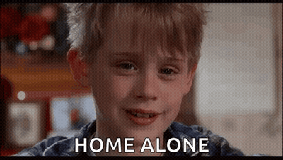 A Young Boy Is Smiling And Saying `` Home Alone '' While Looking At The Camera . GIF