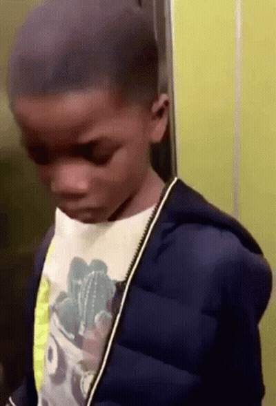A Young Boy Is Standing In An Elevator Wearing A Blue Jacket And A Cactus Shirt . GIF