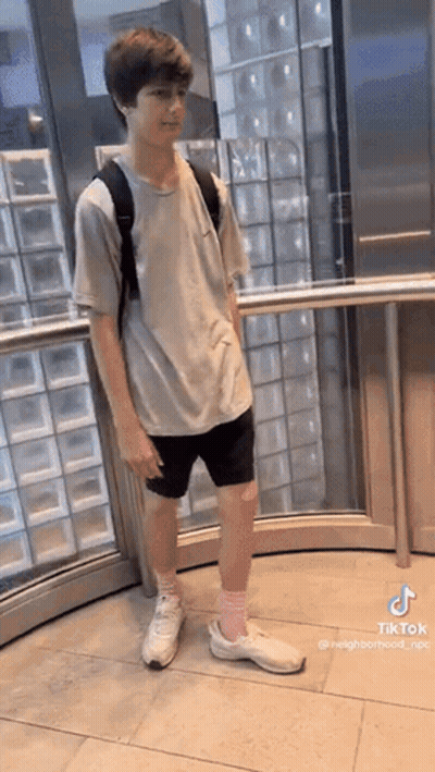 A Young Boy Is Standing In An Elevator Wearing Shorts And A Backpack . GIF