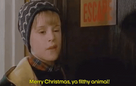 A Young Boy Is Standing In Front Of A Door And Saying `` Merry Christmas , Ya Filthy Animal ! '' . GIF