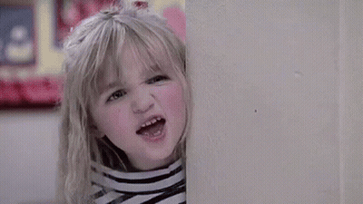 A Young Boy Is Standing In Front Of A Red Door Looking Out The Window . GIF