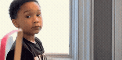 A Young Boy Is Standing In Front Of A Window And Looking At The Camera With A Serious Look On His Face . GIF