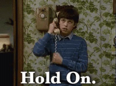 A Young Boy Is Talking On A Telephone With The Words Hold On Written On The Bottom GIF