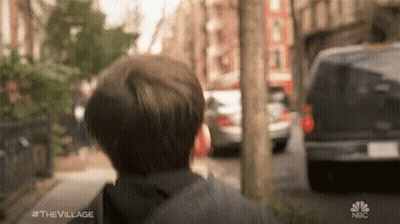 A Young Boy Is Walking Down A Street With A Van Behind Him . GIF