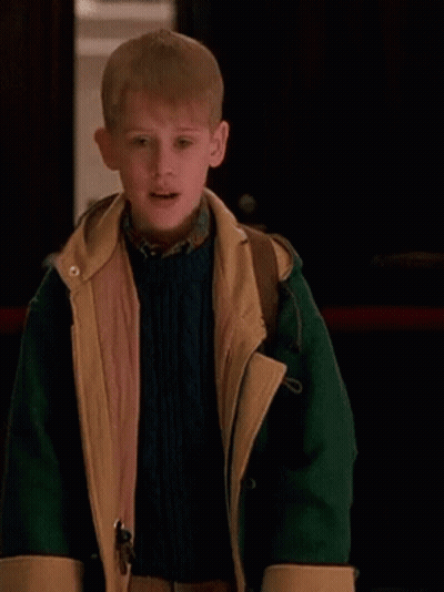 A Young Boy Is Wearing A Green And Yellow Jacket And A Blue Sweater . GIF
