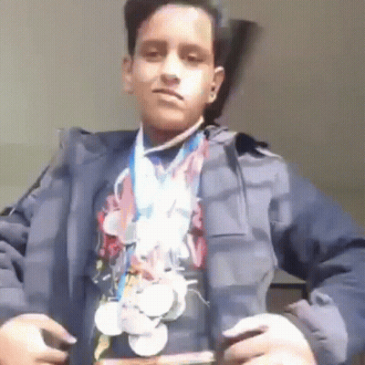 A Young Boy Is Wearing A Jacket And A Medal Around His Neck . GIF